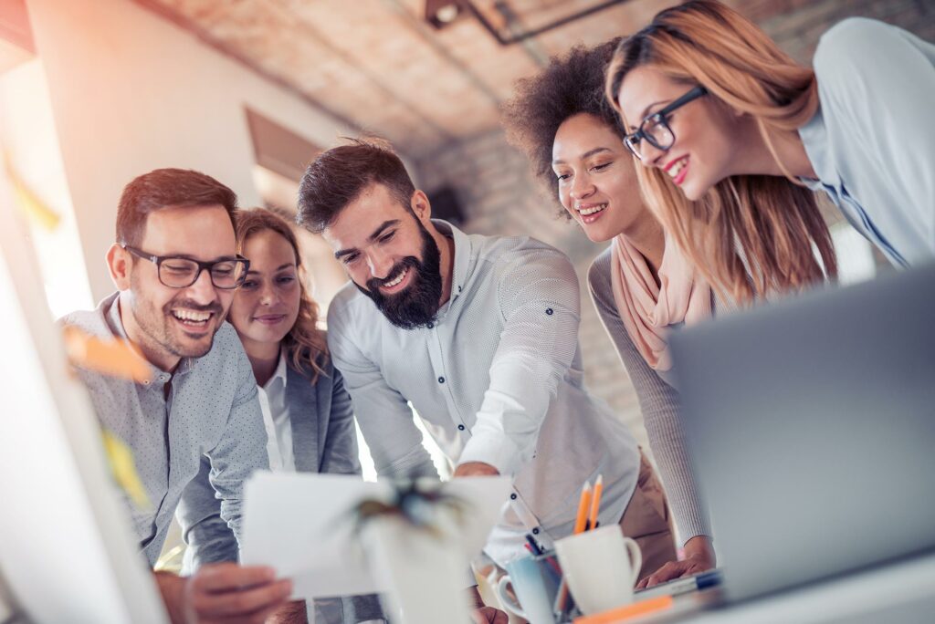 A cheerful group of diverse co-workers collaborating and looking at a laptop screen together.