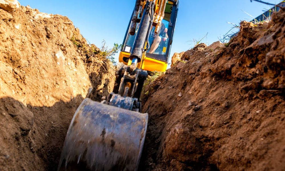 The powerful arm of an excavator digging into the earth, seen from a ground-level perspective.